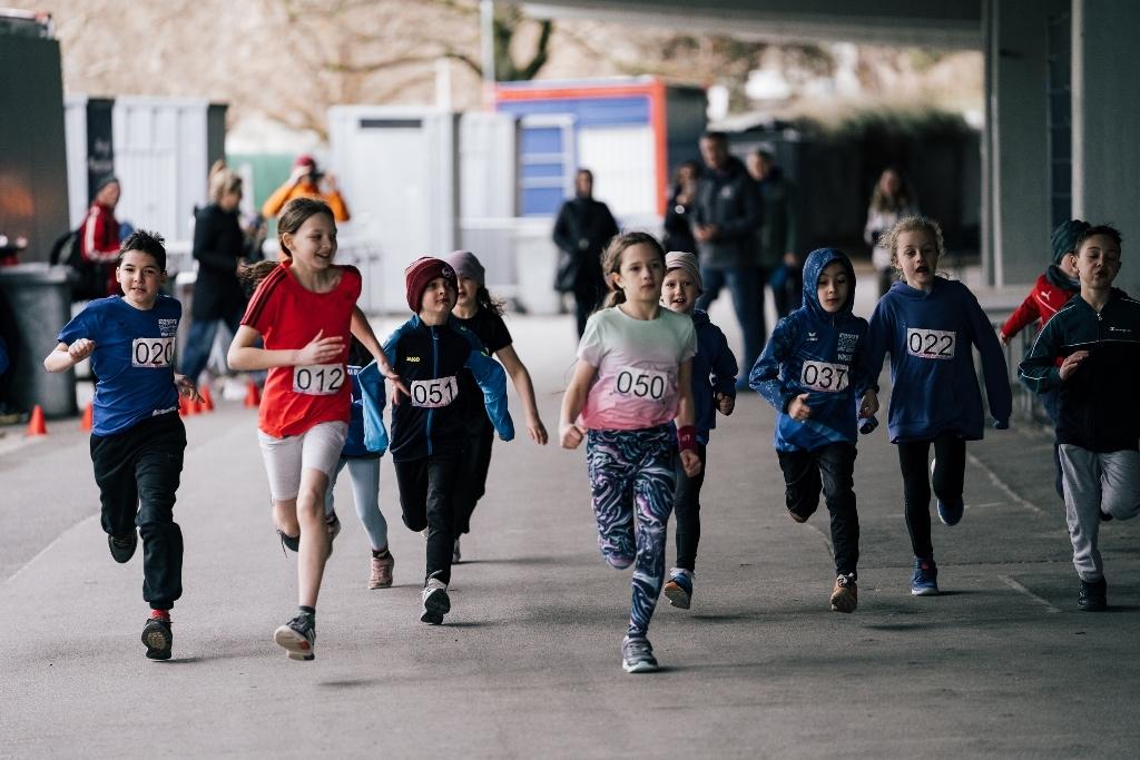 Eine Gruppe von Kindern in Sportkleidung l&auml;uft gemeinsam in einem Wettbewerb, ihre Startnummern gut sichtbar.