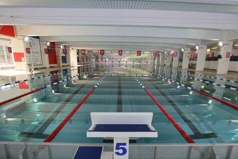 Leeres Schwimmbecken mit Startblock und markierten Bahnen unter heller Beleuchtung.