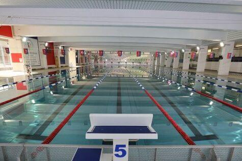 Leeres Schwimmbecken mit Startblock und markierten Bahnen unter heller Beleuchtung.