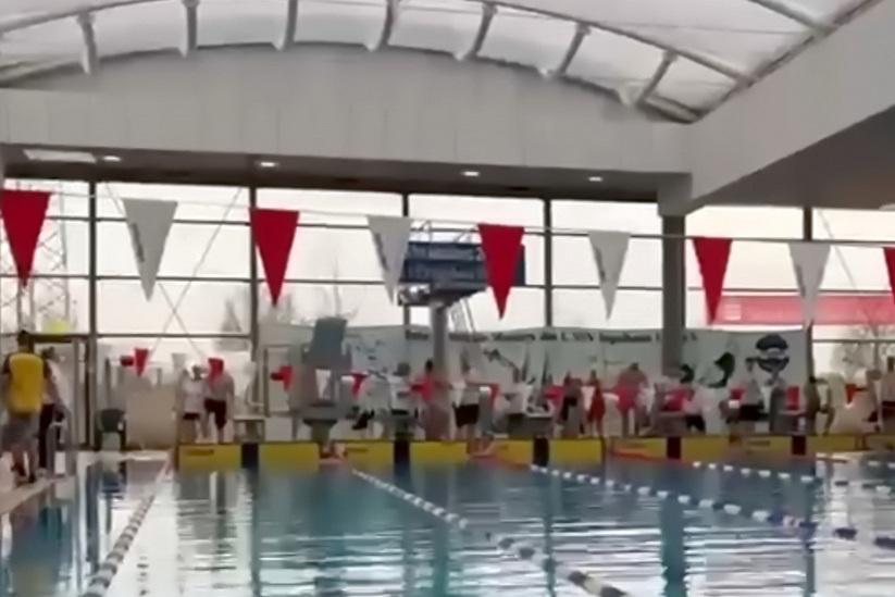Schwimmbecken in einer Halle mit Schwimmern an den Startbl&ouml;cken und bunten Fahnen entlang der Bahn.