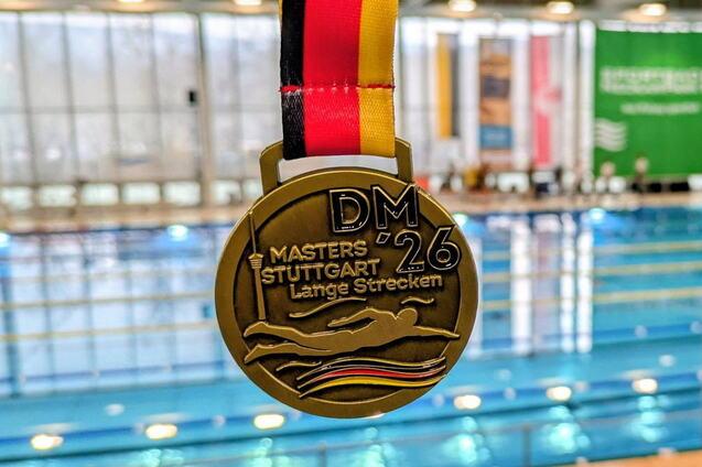 Goldmedaille mit schwarz-rot-gelbem Band, im Hintergrund ein Schwimmbecken der DM Masters in Stuttgart.