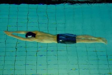 Schwimmer in blauen Shorts taucht kopfirst ins Wasser auf einer Unterwasseraufnahme.