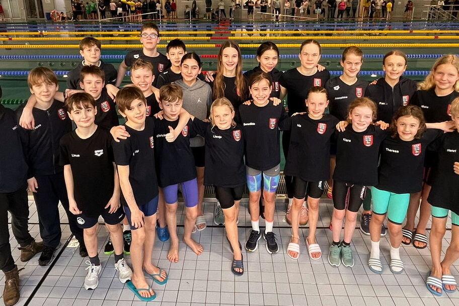 Gruppenselfie von 23 Kindern in Schwimmkleidung am Schwimmbecken, l&auml;chelnd und posierend f&uuml;r die Kamera.