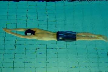 Schwimmer in blauen Shorts taucht kopfirst ins Wasser auf einer Unterwasseraufnahme.