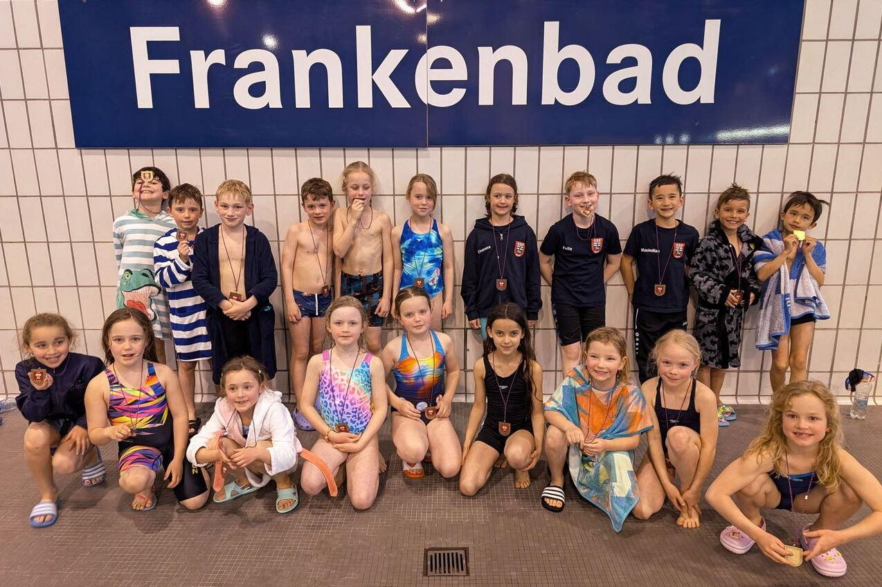 Gruppenfoto von Kindern in Schwimmbekleidung vor dem Schild &bdquo;Frankenbad&ldquo; an einer Schwimmhalle.