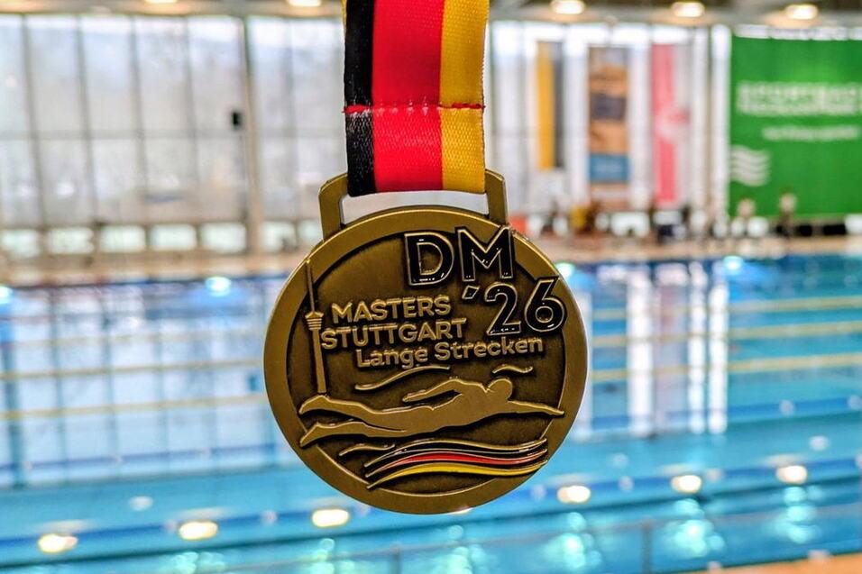 Goldmedaille mit schwarz-rot-gelbem Band, im Hintergrund ein Schwimmbecken der DM Masters in Stuttgart.