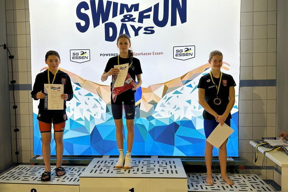 Drei junge Schwimmerinnen stehen auf dem Siegertreppchen bei den Essener Swim and Fun Days mit Medaillen und Urkunden.