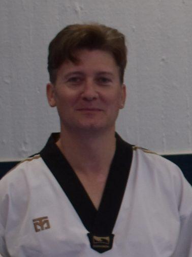 Person in schwarzer und wei&szlig;er Taekwondo-Gewandung steht vor einer hellen Wand. Freundlicher Gesichtsausdruck.