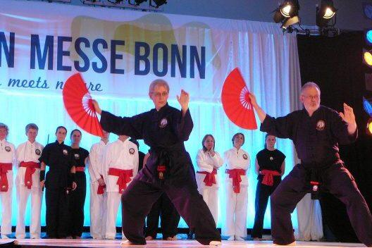 Zwei Kampfk&uuml;nstler in schwarzer Kleidung f&uuml;hren eine Fan-Demonstration auf einer B&uuml;hne bei einer Veranstaltung durch.