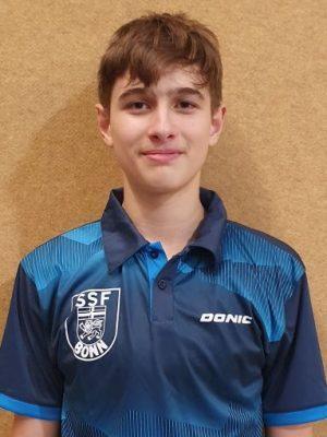 Portr&auml;t eines jungen Mannes mit braunen Haaren, der ein blaues Tischtennis-Trikot mit dem Logo &bdquo;SSF Bonn&ldquo; tr&auml;gt.