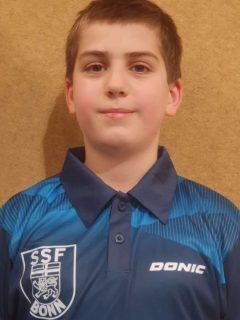 Portr&auml;t eines Jungen in einem blauen Trikot mit dem Logo &bdquo;SSF Bonn&ldquo; und dem Schriftzug &bdquo;DONIC&ldquo;. Hintergrund einfarbig.