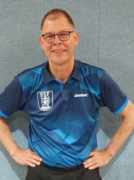 Mann in blauer Sportkleidung mit Aufdruck &bdquo;SSF Borken&ldquo; steht l&auml;chelnd vor einer grauen Wand.