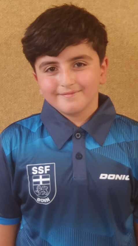 Junge mit dunklen Haaren trägt ein blaues Sporttrikot mit SSF Bonn-Logo vor einem neutralen Hintergrund.