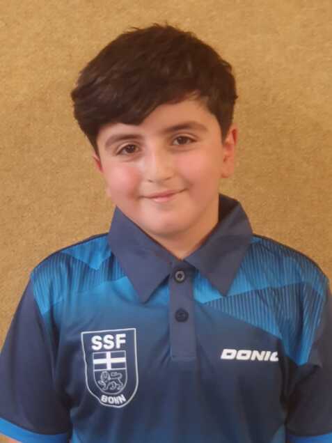 Junge mit dunklen Haaren tr&auml;gt ein blaues Sporttrikot mit SSF Bonn-Logo vor einem neutralen Hintergrund.