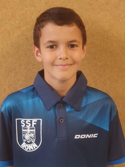 Junger Tischtennisspieler mit kurzem, lockigem Haar in einem blauen Trikot mit dem Logo &bdquo;SSF Bonn&ldquo; im Portrait.