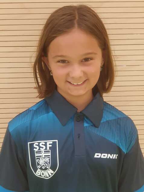 L&auml;chelndes M&auml;dchen in blauer Sporttrikots mit Logo auf hellem, gestreiften Hintergrund.