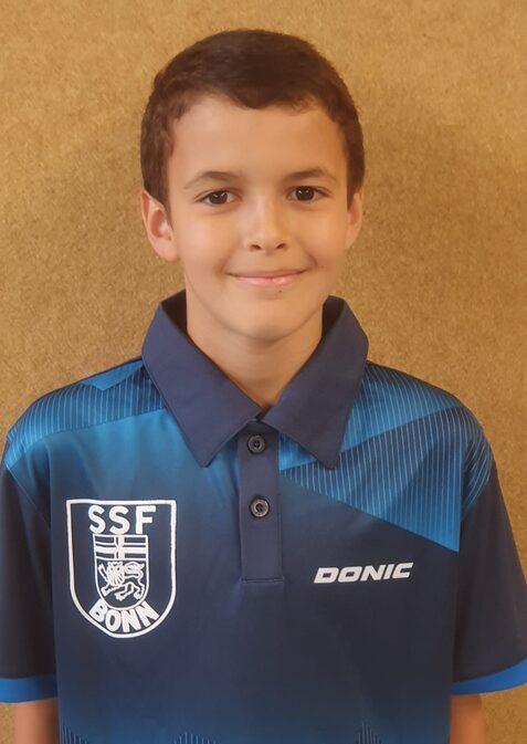 Junger Tischtennisspieler mit kurzem, lockigem Haar in einem blauen Trikot mit dem Logo „SSF Bonn“ im Portrait.