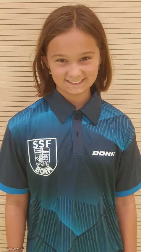 Lächelndes Mädchen in blauer Sporttrikots mit Logo auf hellem, gestreiften Hintergrund.