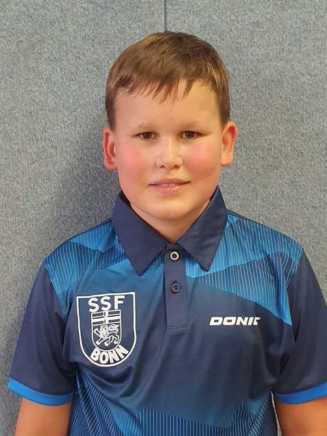 Portr&auml;t eines jungen Tischtennisspielers in einem blauen Teamtrikot mit Vereinslogo und l&auml;chelndem Gesicht.