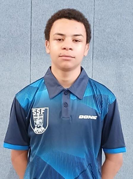 Junger Sportler in einem blauen Tischtennis-Trikot mit Logo, vor einer grauen Wand.