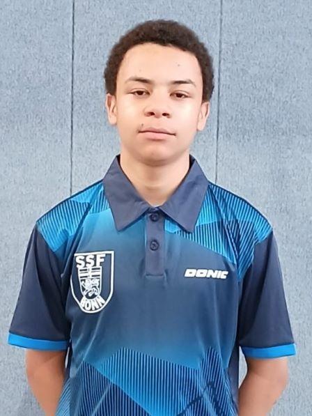 Junger Sportler in einem blauen Tischtennis-Trikot mit Logo, vor einer grauen Wand.