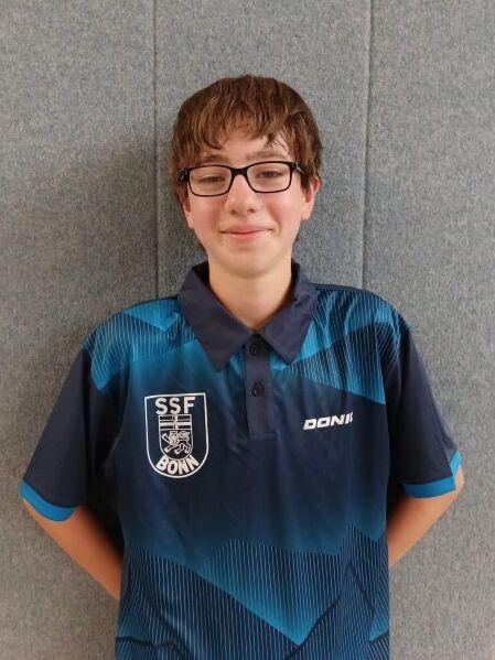 Junger Tischtennisspieler mit Brille tr&auml;gt ein blaues Vereinshemd vor einem grauen Hintergrund.