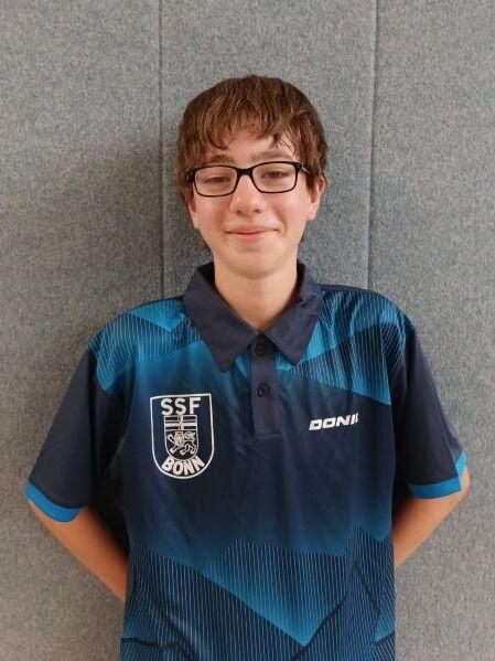 Junger Tischtennisspieler mit Brille tr&auml;gt ein blaues Vereinshemd vor einem grauen Hintergrund.