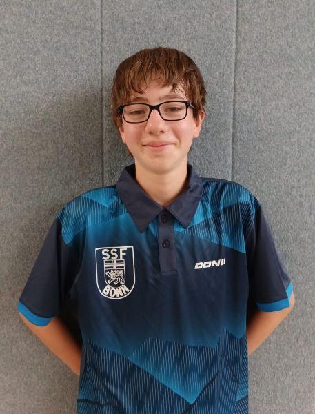 Junger Tischtennisspieler mit Brille trägt ein blaues Vereinshemd vor einem grauen Hintergrund.
