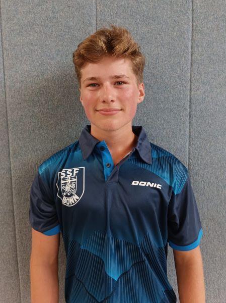 Portr&auml;t eines Jugendlichen mit blonden Haaren, in einem blau-schwarzen Tischtennis-Trikot mit Vereinslogo.