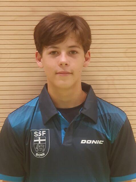 Junger Tischtennisspieler mit braunen Haaren tr&auml;gt ein blau-schwarz gestreiftes Polo-Shirt mit Vereinslogo.