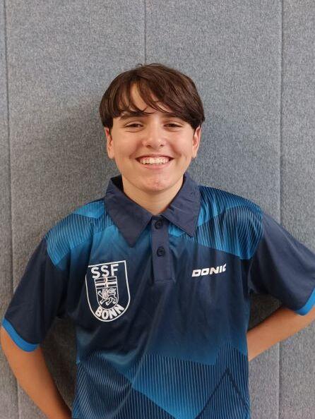 Junger Sportler mit l&auml;chelndem Gesicht, in einem blauen Tischtennisshirt mit Logo des SSF Bonn.