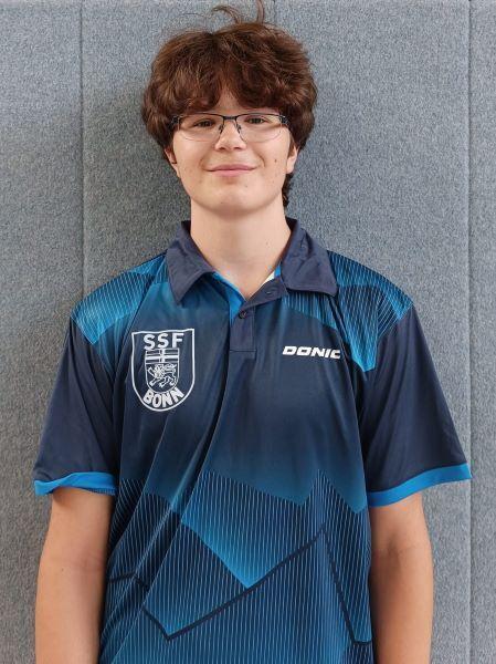 Junger Mann mit Brille tr&auml;gt ein blaues Sporttrikot mit dem Logo &bdquo;SSF Bonn&ldquo; vor grauem Hintergrund.