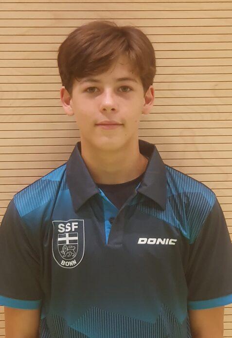 Junger Tischtennisspieler mit braunen Haaren trägt ein blau-schwarz gestreiftes Polo-Shirt mit Vereinslogo.