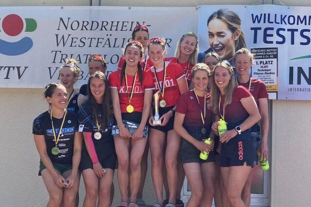 Gruppe von zehn Frauen auf einem Winners Podest mit Medaillen nach einem Triathlon-Wettbewerb, freundlich l&auml;chelnd.