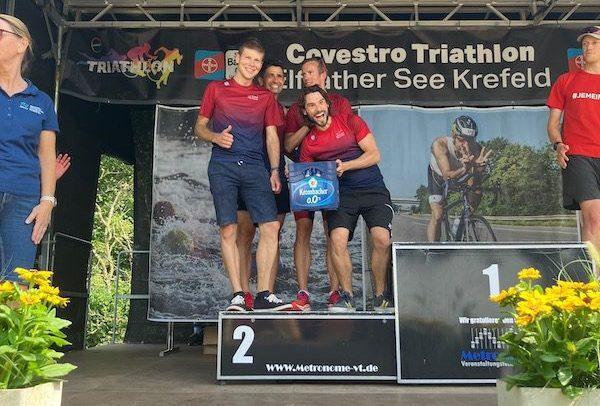 Drei Athleten stehen auf dem Podium des Covestro Triathlons, der zweite Platz ist eher sichtbar.