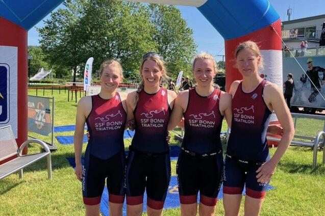 Vier Frauen in Triathlonanz&uuml;gen posieren vor einem bunten Zielbogen des Triathlon Verbands Nordrhein-Westfalen.