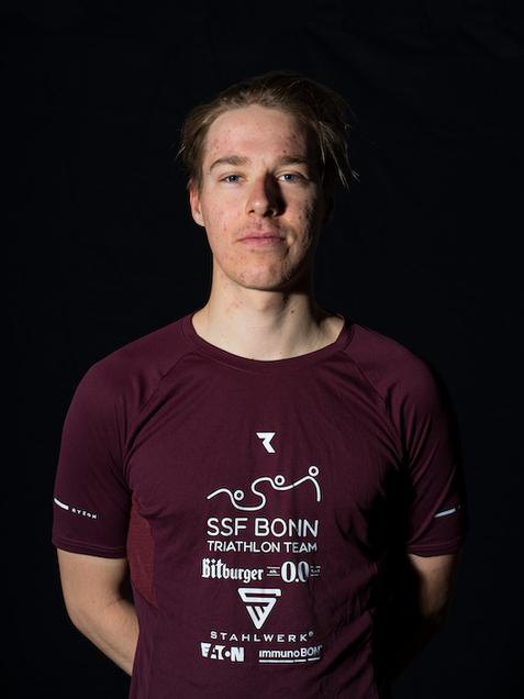 Portr&auml;t eines jungen Mannes im Triathlon-Trikot des SSF Bonn, mit neutralem Ausdruck vor schwarzem Hintergrund.
