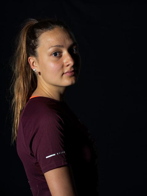 Portr&auml;t einer jungen Frau mit langen, offenen Haaren, in einem dunkelrot-blauen Sportshirt, vor schwarzem Hintergrund.