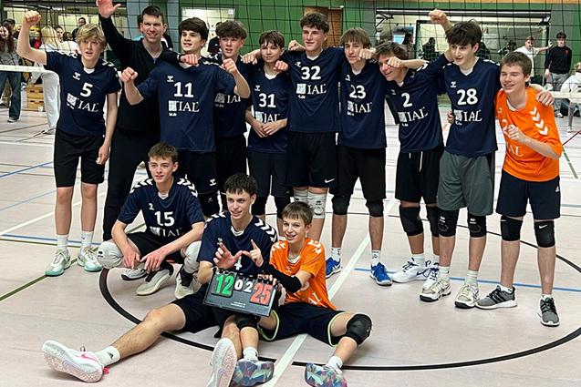 Gruppe junger Volleyballspieler posiert nach einem Spiel, halten ein Ergebnisbrett mit 12:25 in einer Sporthalle.