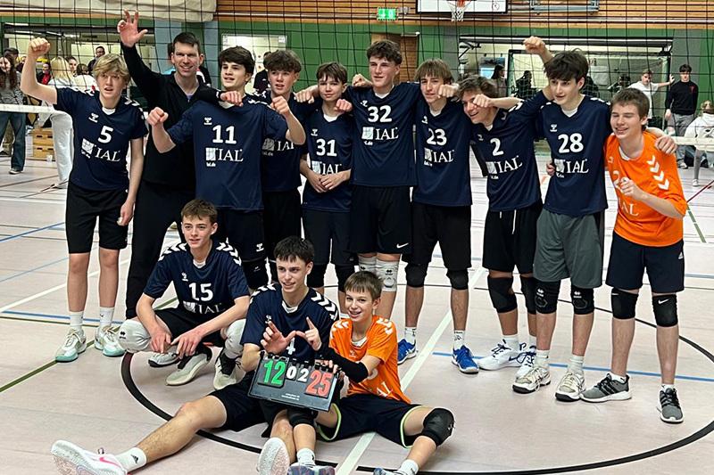 Gruppe junger Volleyballspieler posiert nach einem Spiel, halten ein Ergebnisbrett mit 12:25 in einer Sporthalle.