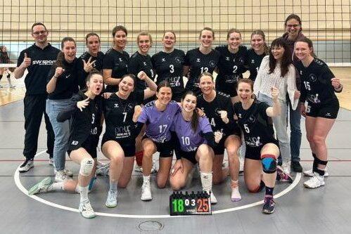 Mannschaftsfoto einer weiblichen Volleyballmannschaft mit Trainer, l&auml;chelnd und jubelnd nach einem Spiel.