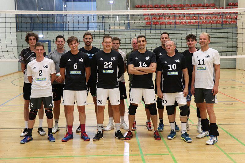 Gruppe von zw&ouml;lf Volleyballspielern in passenden Trikots, auf einem Spielfeld vor einem Netz.