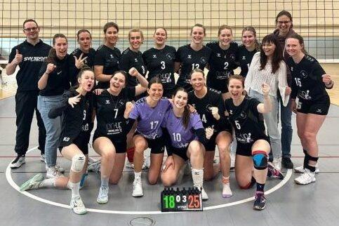Mannschaftsfoto einer weiblichen Volleyballmannschaft mit Trainer, l&auml;chelnd und jubelnd nach einem Spiel.