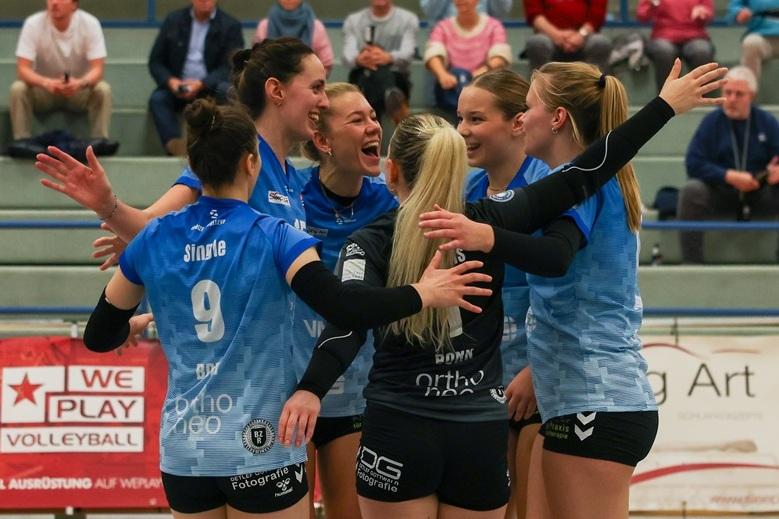 Sechs Volleyballspielerinnen jubeln gemeinsam in einem Sporthalle, l&auml;cheln und feiern einen erfolgreichen Punkt.