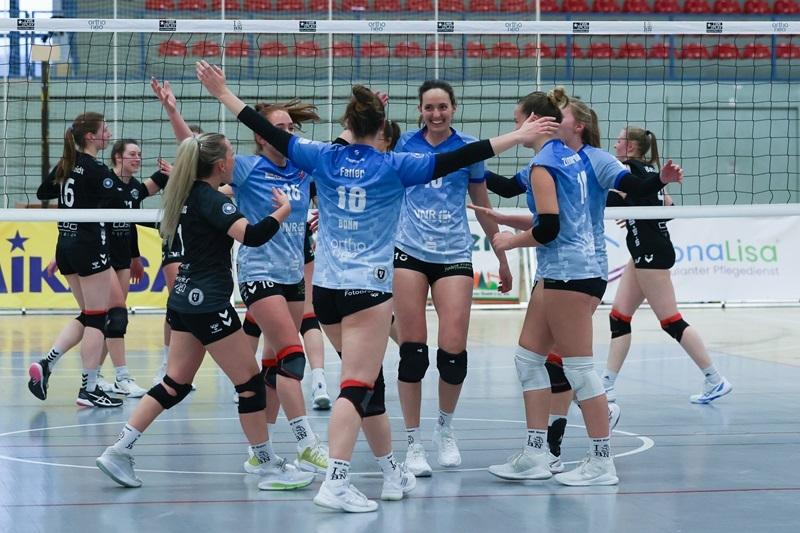 Gruppenkonferenz von Volleyballspielerinnen in blauen Trikots, die sich jubelnd umarmen. Voller Freude nach einem Punkt.
