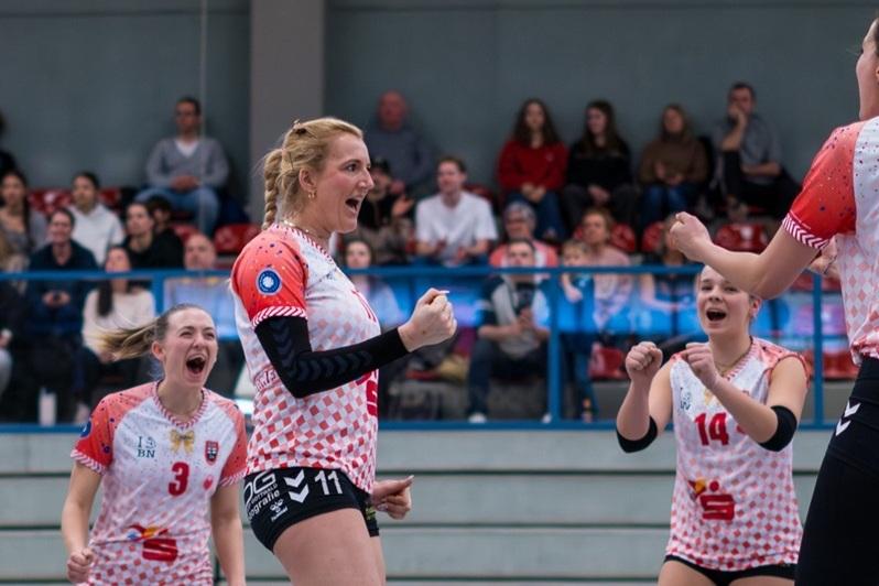 Vier Volleyballspielerinnen jubeln lautstark auf dem Spielfeld, im Hintergrund ist ein Publikum zu sehen.