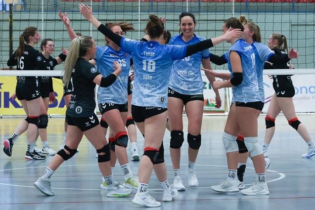 Gruppenkonferenz von Volleyballspielerinnen in blauen Trikots, die sich jubelnd umarmen. Voller Freude nach einem Punkt.