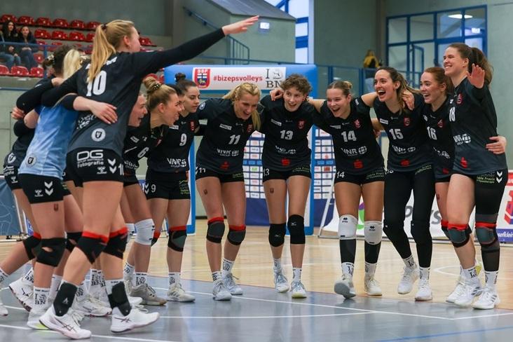 Zehn Sportlerinnen feiern im Kreis auf dem Volleyballfeld, in einheitlicher Teamkleidung, Stimmung ist ausgelassen.