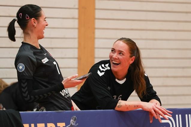 Zwei lachende Handballspielerinnen sitzen an der Bank, die eine h&auml;lt ein Smartphone in der Hand.
