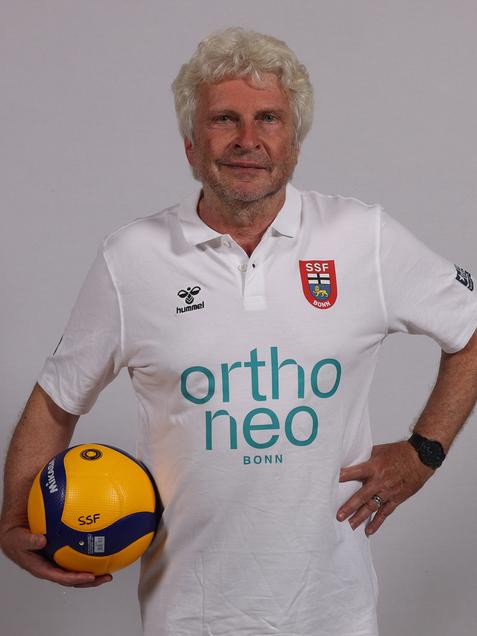 &Auml;lterer Mann h&auml;lt einen Volleyball in der Hand, tr&auml;gt ein wei&szlig;es Polo-Shirt mit dem Logo "SSF Bonn".